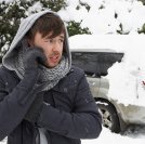 Young man in snow with broken down car